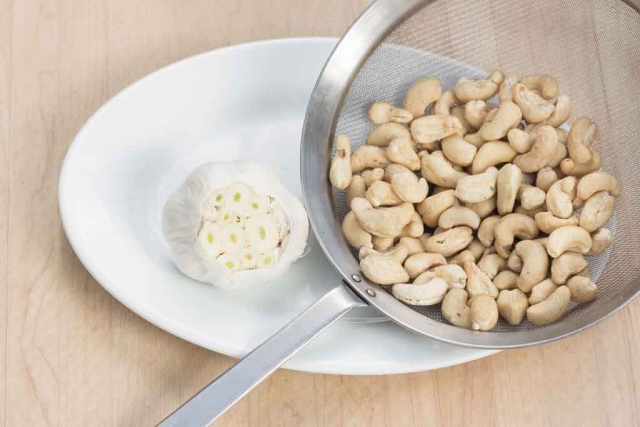 Cut of top of garlic bulb; rinse and drain cashews.