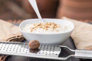 Creamy Almond Ricotta in a small bowl garnished with toasted almonds, nutmeg and fresh ground pepper behind.