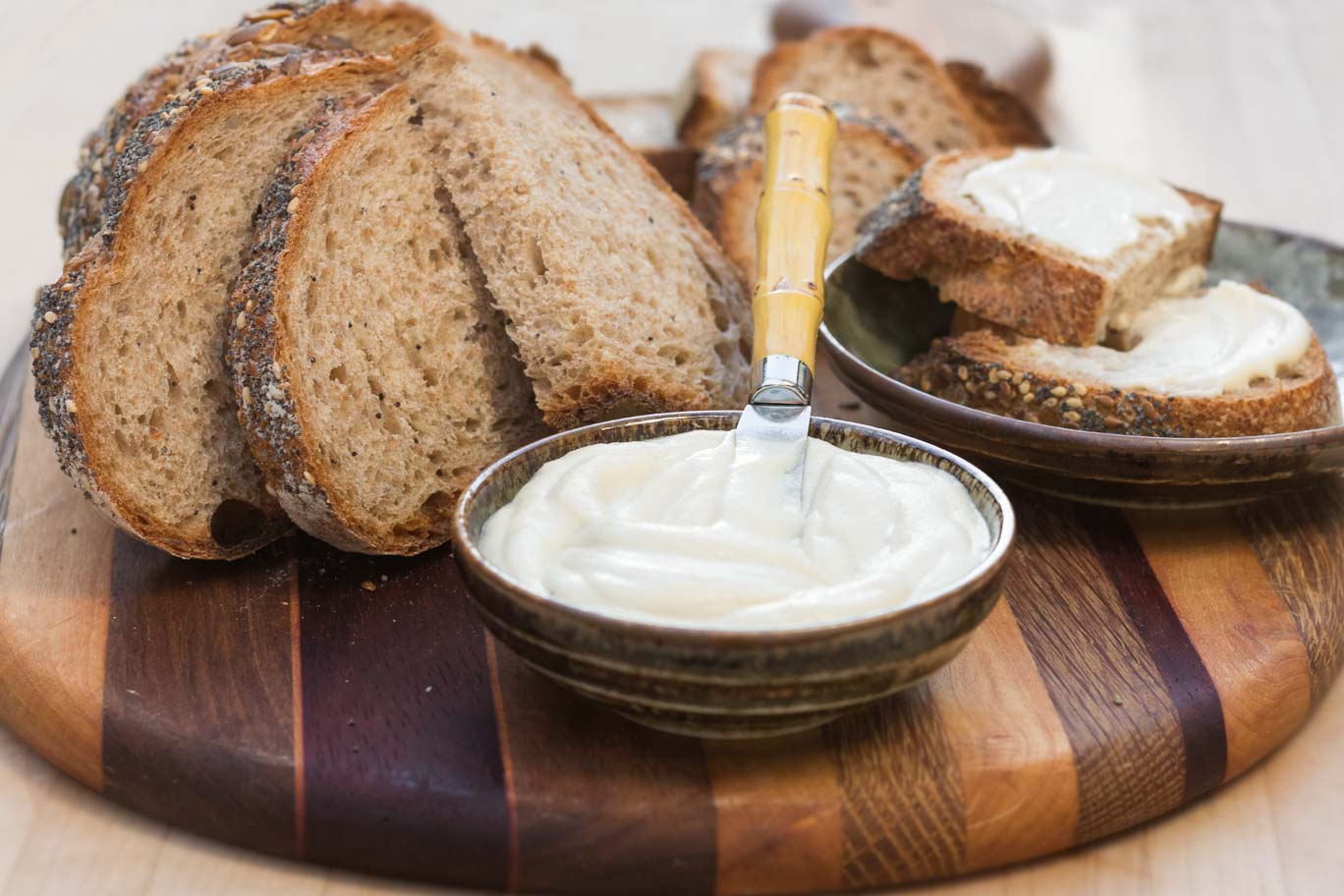 Luscious Oil-free Vegan Butter swirled in a small bowl served on a wooden board with whole grain bread on a wooden board