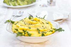 White bowl on a white tablecloth with oil-free vegan Mashed Potatoes garnished with parsley and black pepper