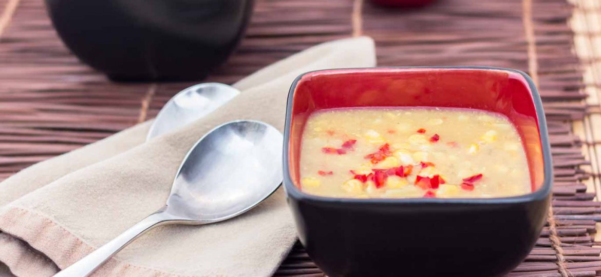 Black and red square bowl with Early Fall Corn Chowder on a bamboo placemat.