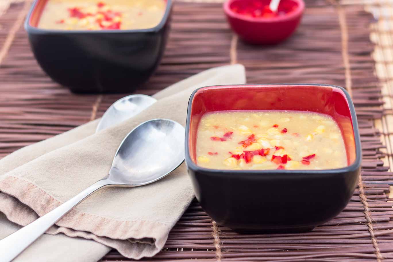 Black and red square bowl with Early Fall Corn Chowder on a bamboo placemat.