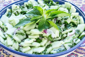 Blue rimmed shallow bowl with Cool Peppermint and Cucumber Salad garnished with fresh whole leaf peppermint in the center.