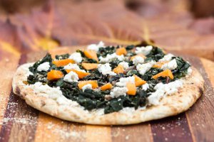 Swiss Chard & Creamy Almond Ricotta Pizza on a wood serving board.