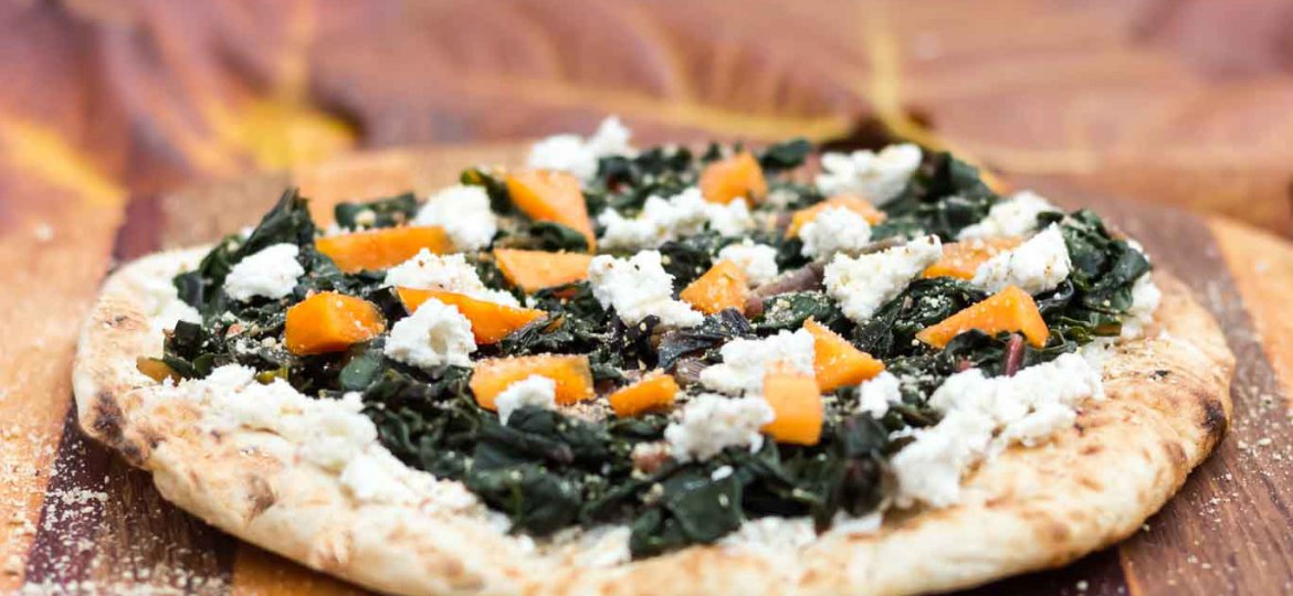 Swiss Chard & Creamy Almond Ricotta Pizza on a wood serving board.