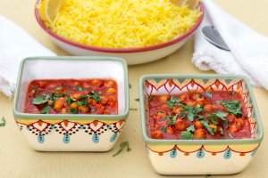 Two square hand-painted bowls with Moroccan Inspired Warm-Spiced Chickpeas and a shallow bowl with saffron rice in back.