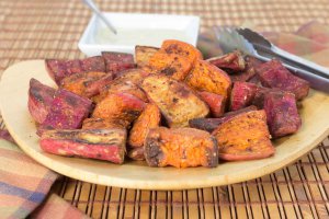 Bamboo rounded platter with Oil-free Spice Roasted Sweet Potatoes on a wooden placemat and oil-free vegan mayonnaise in a small white bowl.