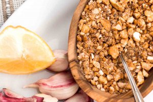 Salt-free Cashew Spice Blend in a small olivewood bowl on a white plate with garlic cloves and a lemon wedge.