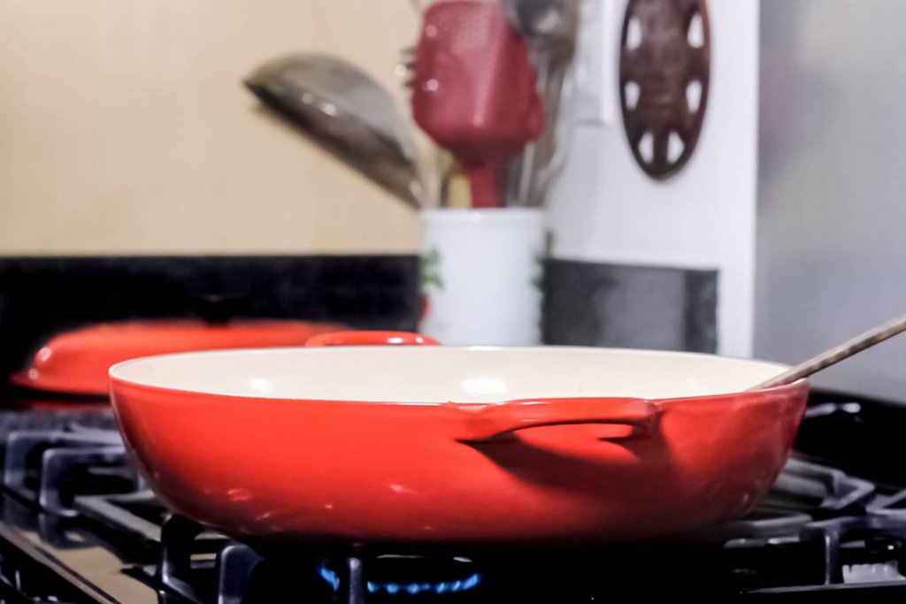 Le Creuset 5qt (3.2L) Braiser on a lit gas burner stove with the gas burner on and the domed lid behind on the counter.