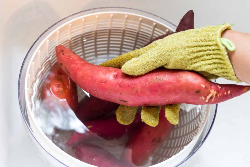 Salad spinner bowl with sweet potatoes. Scrubbing the sweet potato skin.