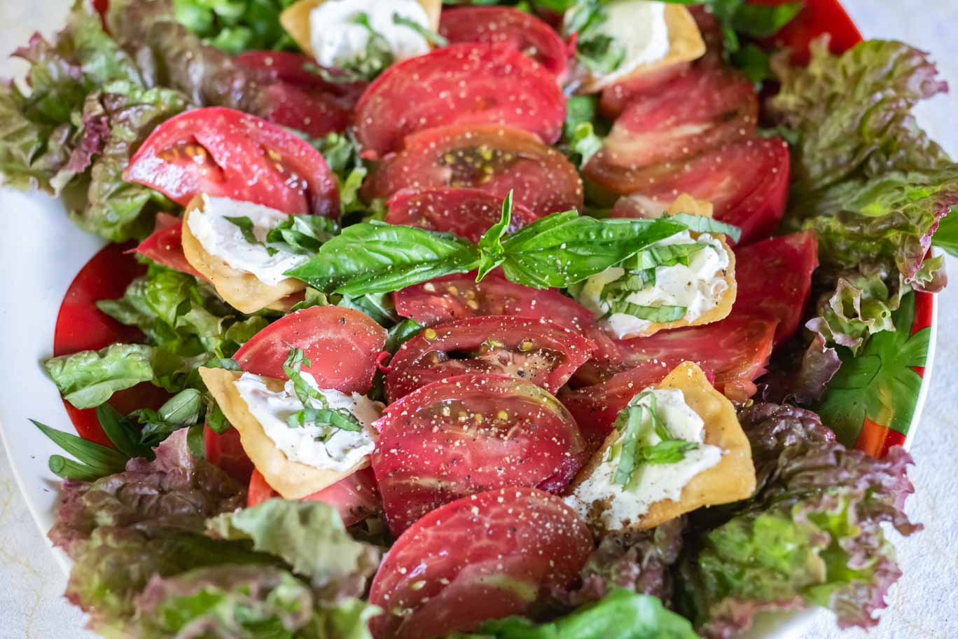 Clsoe-up view of Heirloom Tomato & Basil Salad garnished with black pepper and oil-free baked flatbread with almond ricotta or almond cream cheese