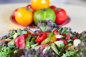 Summer Tomatoes & Avocado Salad Close up view of Summer Tomatoes & Avocado Salad on bed of red leaf lettuce (Lollo Rosso) with whole tomatoes behind.