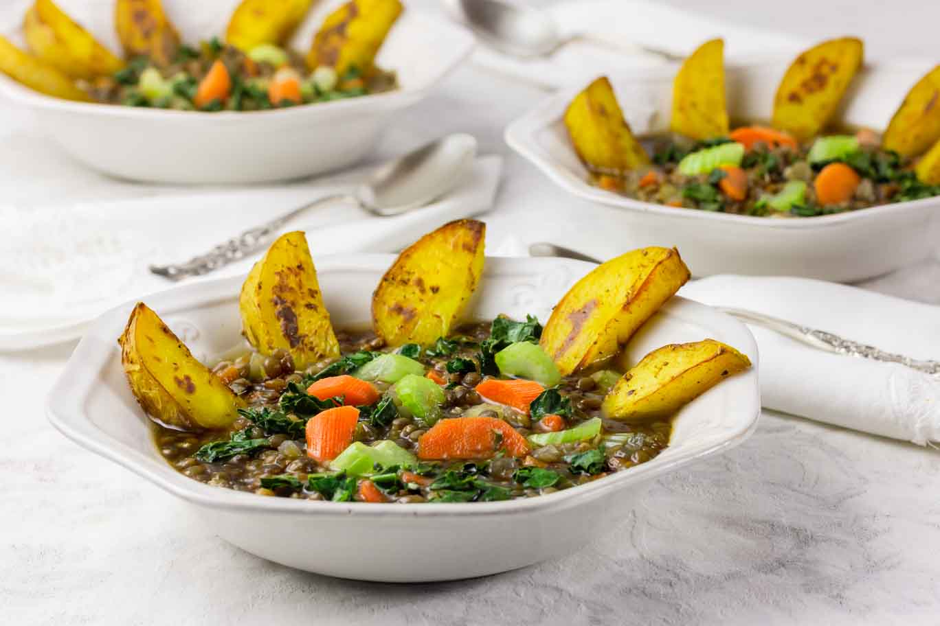 3 white bowls of Mirepoix Mirepoix lentil soup with vibrant vegetables andwith roasted potatoes