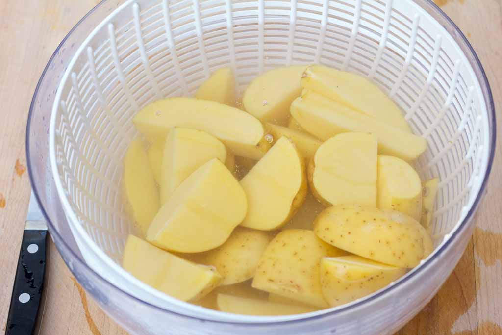 Salad spinner bowl filled with clean water to rinse the cut potatoes