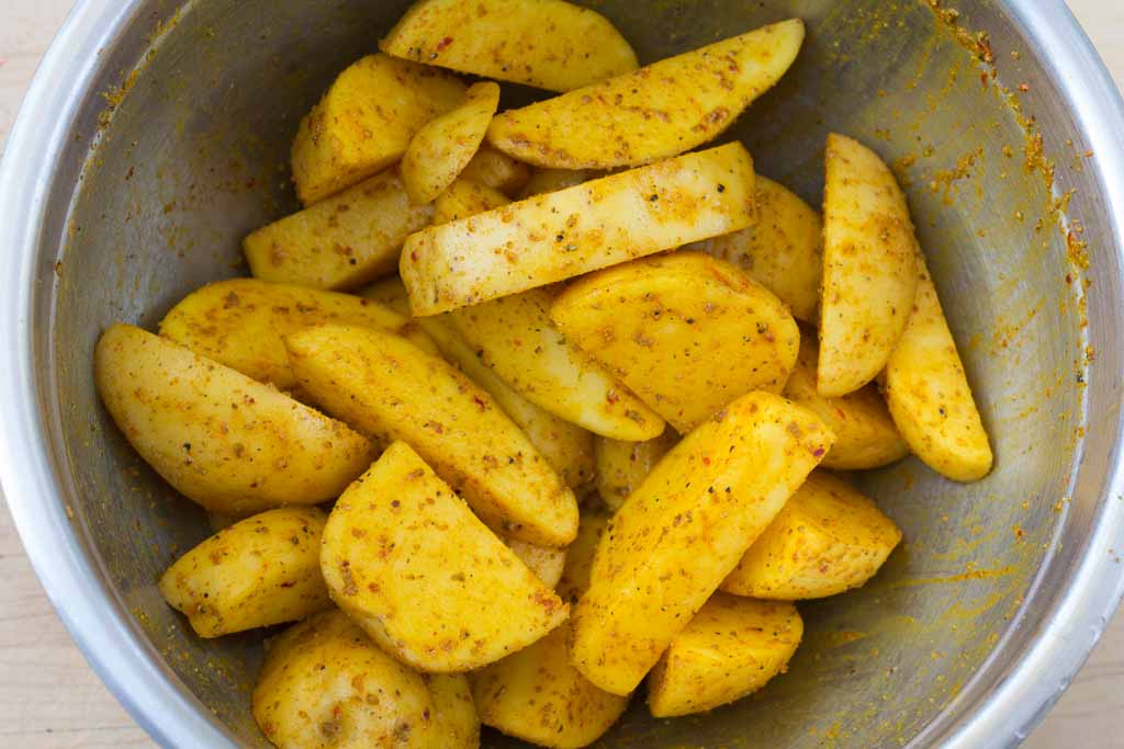 Stainless steel bowl with cut potatoes and spices