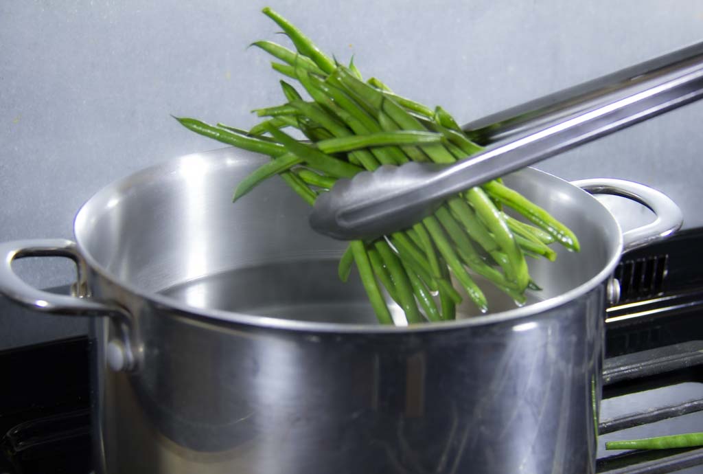 Green beans held with tongs dropping into boiling water