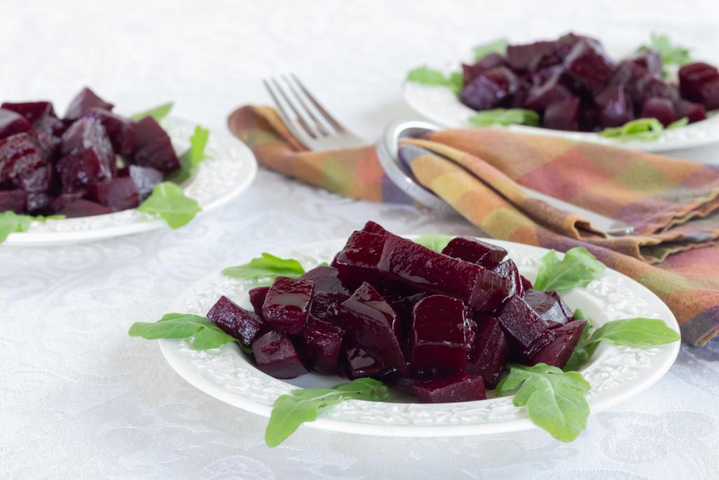 Braised beets on a white Wedgewood plate garnished with arugula with 2 additional plates behind