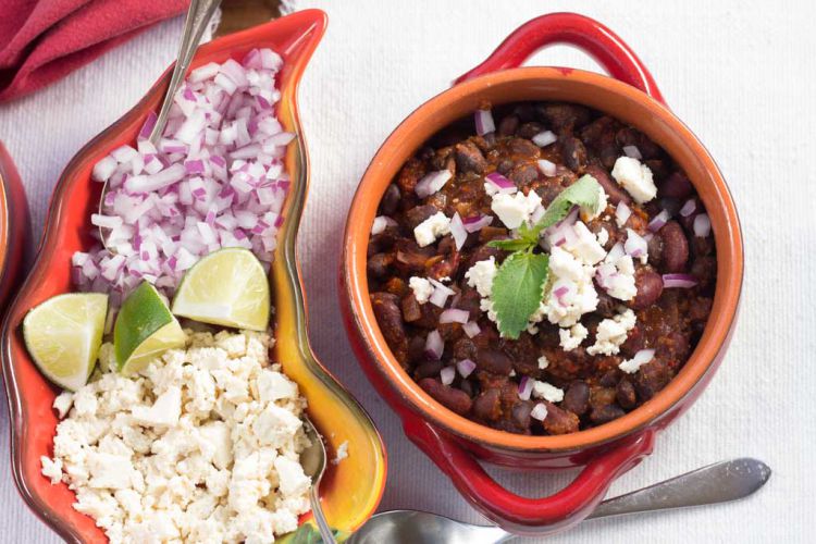 Garnishes: Red and yellow dish with red onion, vegan feat and lime slices and bowl of Chile Bean Chili