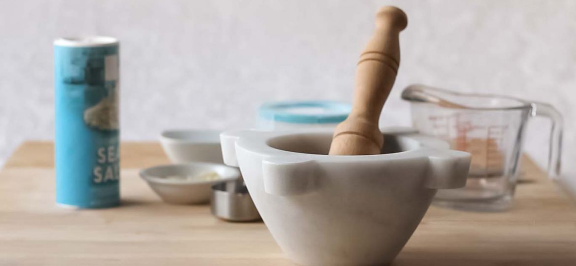 Marble mortar & pestle on a cutting board with prep tools and ingredients behind