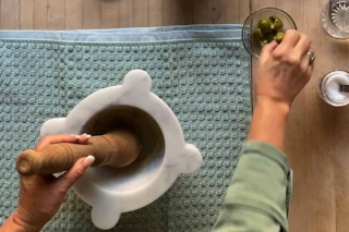 Marble mortar with towel underneath on a board and a small bowl of pitted olives