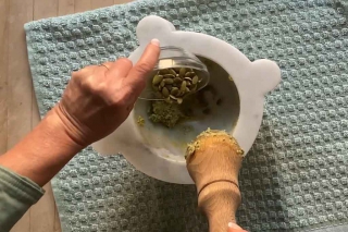 Pouring pumpkin seeds from small bowl into the marble mortar on a board