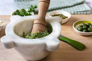 Oil-free Vegan Parsley pesto in the marble mortar with the wood pestle on a cutting board small bowls of Castelvetrano olives, pumpkin seeds and parsley leaves.